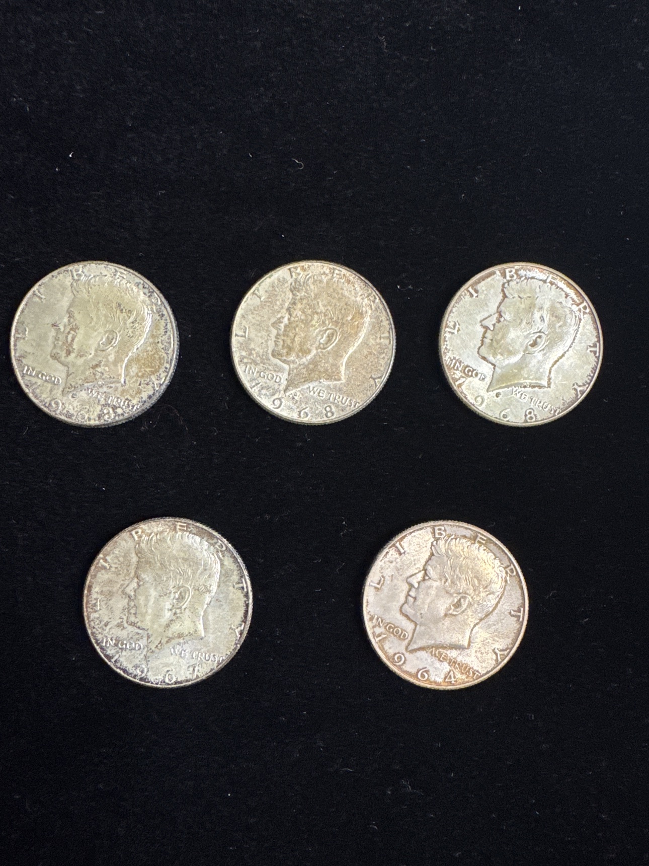 Obverse view of five circulated Kennedy half dollars dated 1964, 1967, and 1968