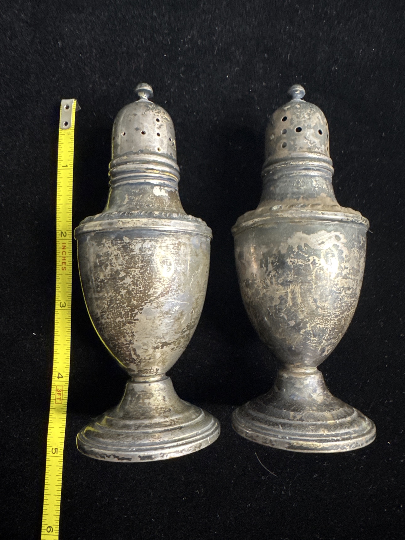 Pair of sterling silver salt and pepper shakers beside a tape measure showing their height