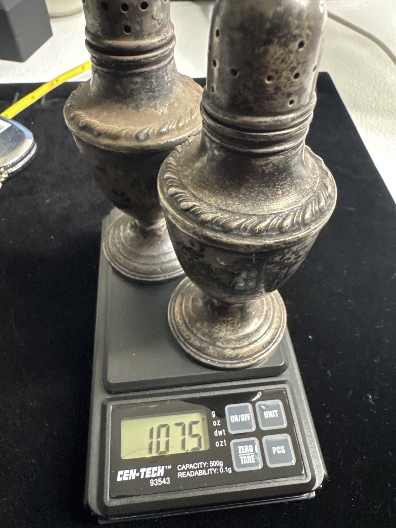 Pair of sterling silver salt and pepper shakers on a scale showing 107.5 grams total